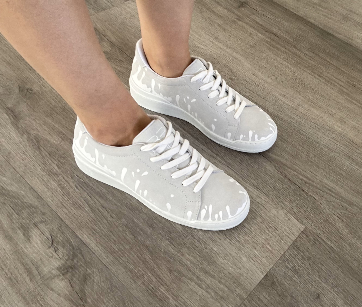 White suede low-top sneakers with exclusive printed white drops design and white soles on wooden floor