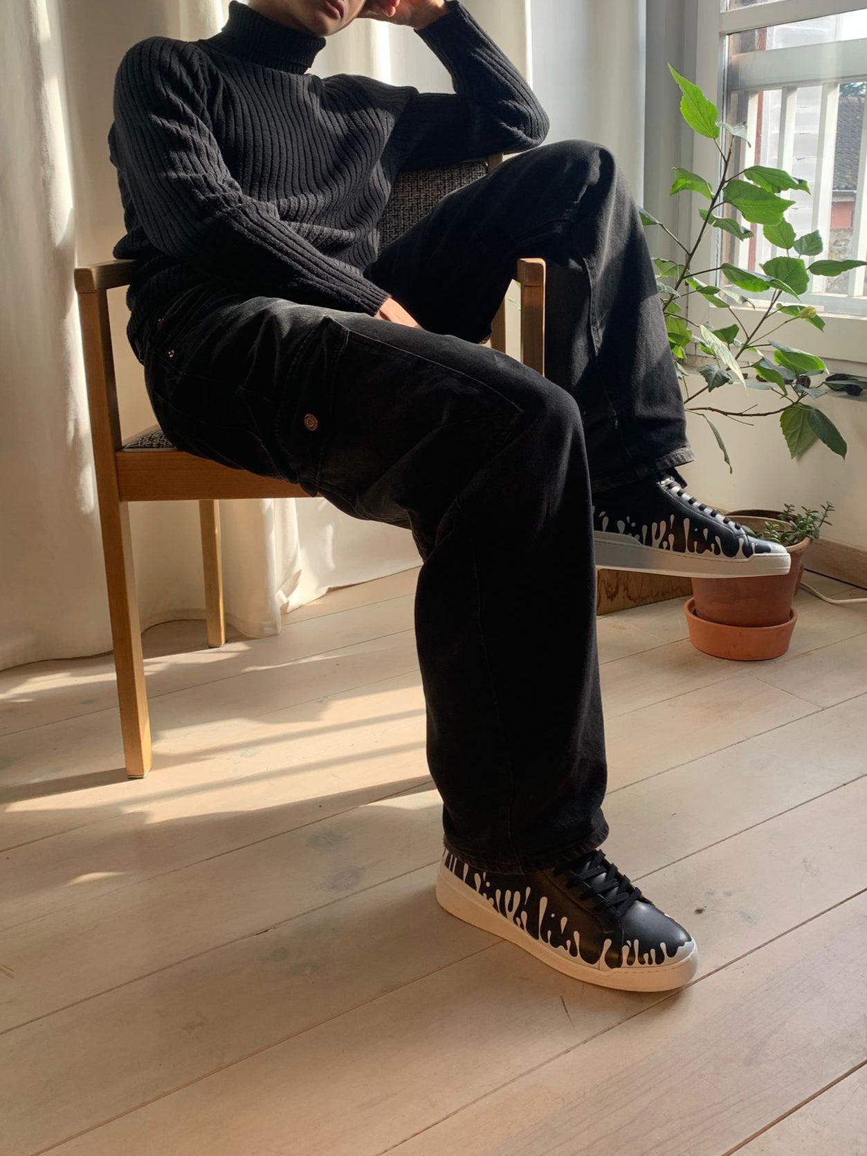 Pair of black Nappa leather mid-top sneaker with exclusive printed white drops design and white sole, worn with black jeans