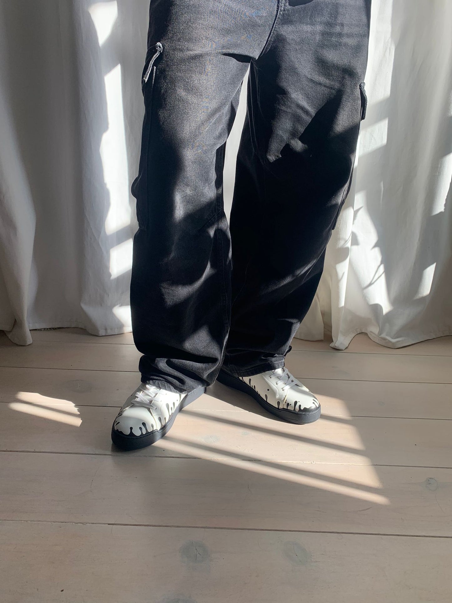 White Nappa leather low-top sneakers with exclusive printed black drops design and black soles, worn on model with back jeans