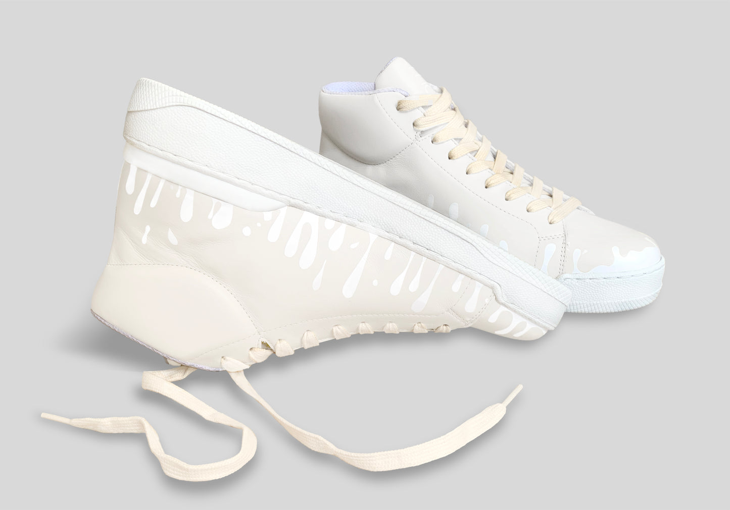 Upside down view of pair of cream Chrome-free Nappa leather mid-top sneakers with exclusive printed white drops design and white soles