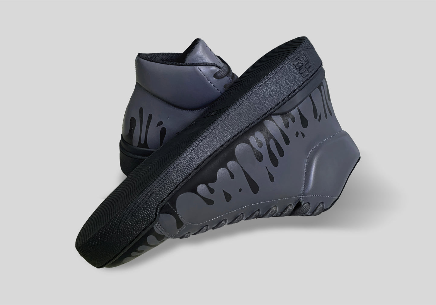Upside down view of pair of dark grey Chrome-free Nappa leather mid-top sneakers with exclusive printed black drops design and black soles