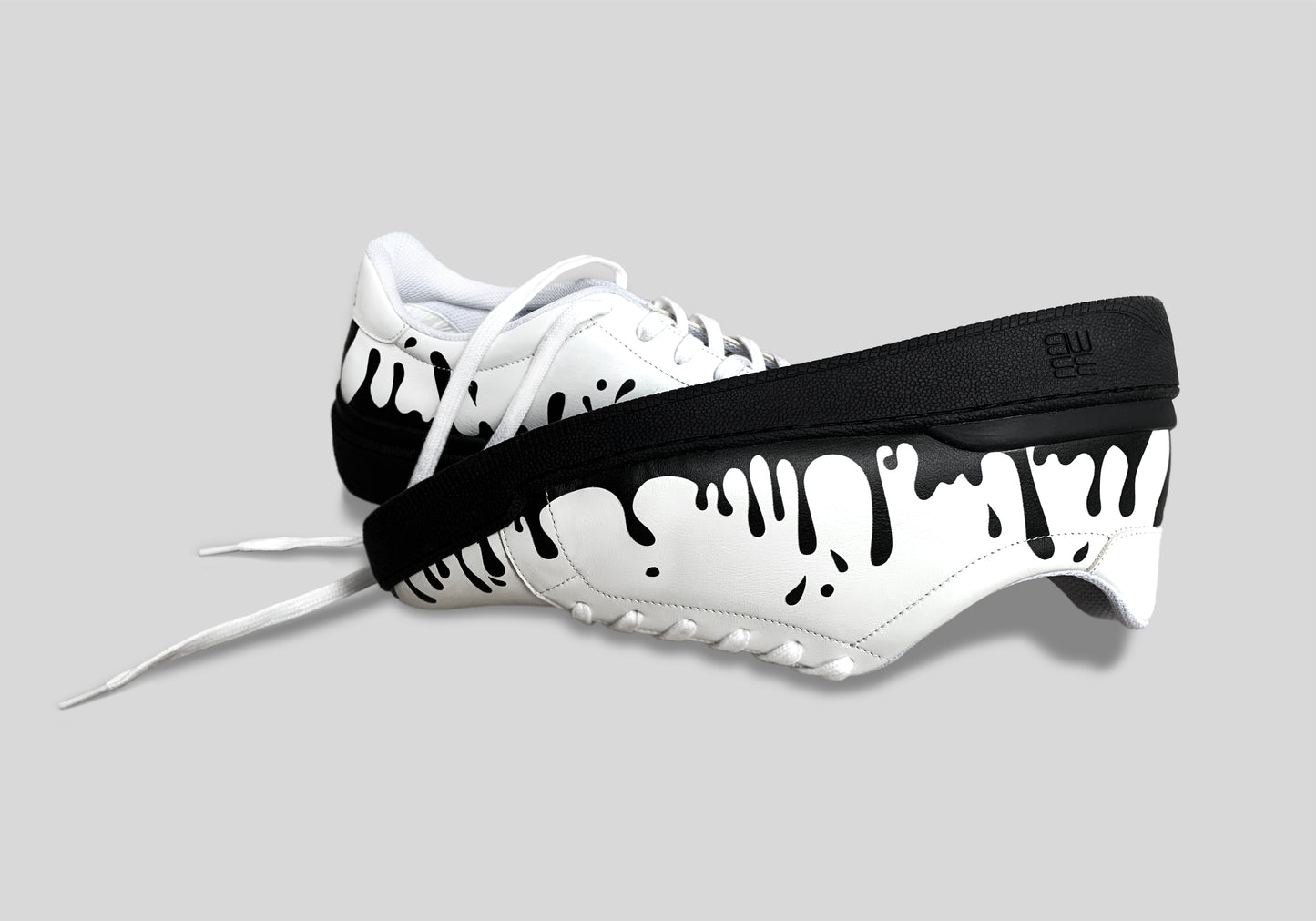 Upside down view of pair of white Nappa leather low-top sneakers with exclusive black drops design on black soles