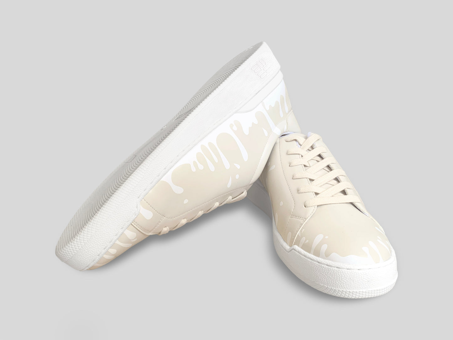 Upside down view of pair of cream Chrome-Free Nappa leather low-top sneakers with exclusive printed white drops design and white soles
