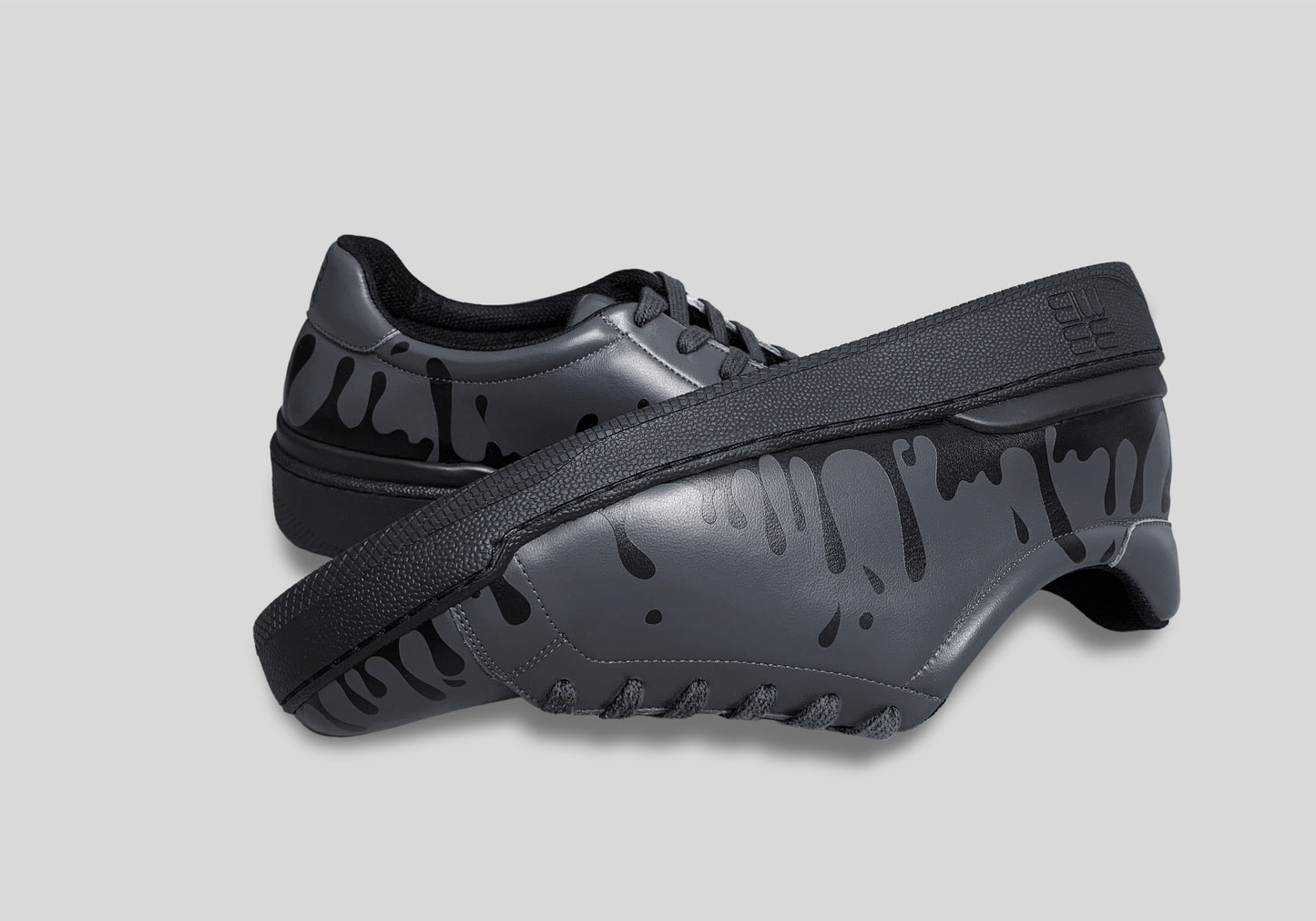 Upside down view of pair of dark grey Chrome-free Nappa leather low-top sneakers with exclusive printed black drops design and black soles