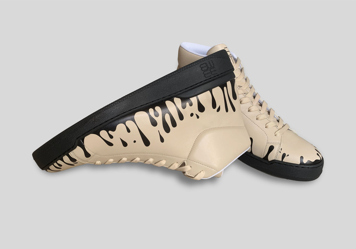 Upside down view of pair of beige Nappa leather mid-top sneakers with exclusive printed black drops design and black soles