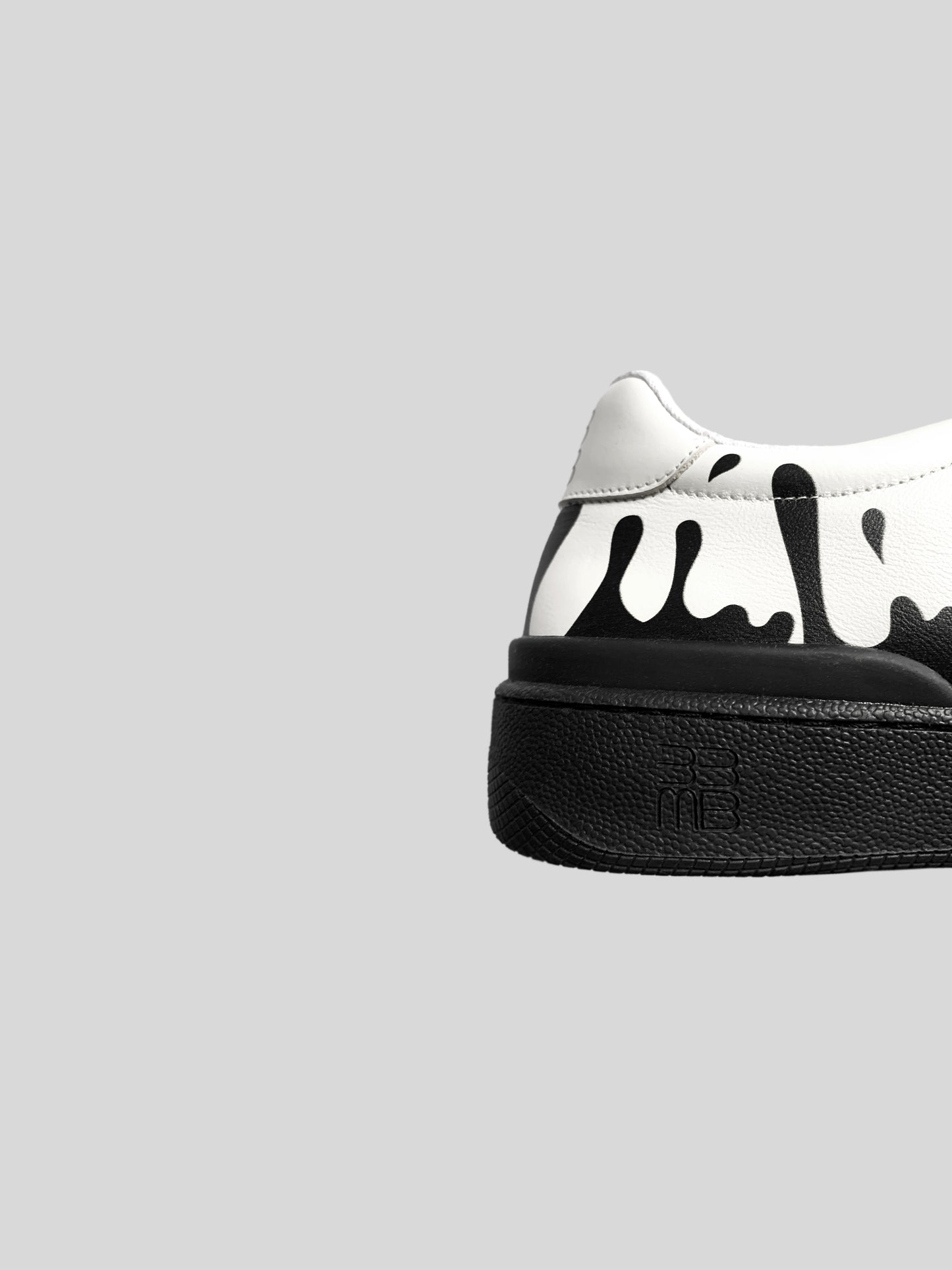 Back side view of white Nappa leather low-top sneakers with exclusive printed black drops design and black soles