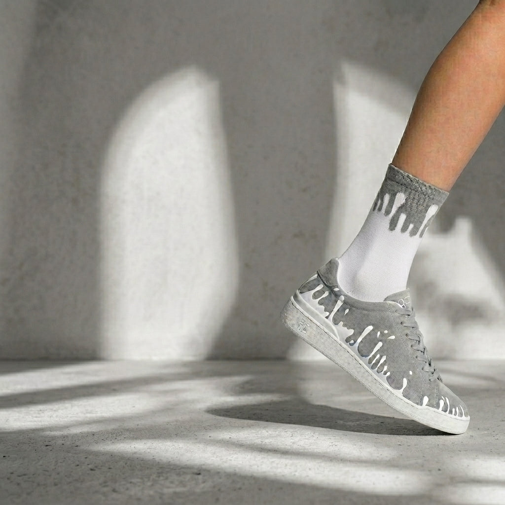 Person wearing 33MB Splash gray sneakers and socks with  Zero Gravity® signature motif of drops moving upward symbolizing hope on a concrete floor with shadows.