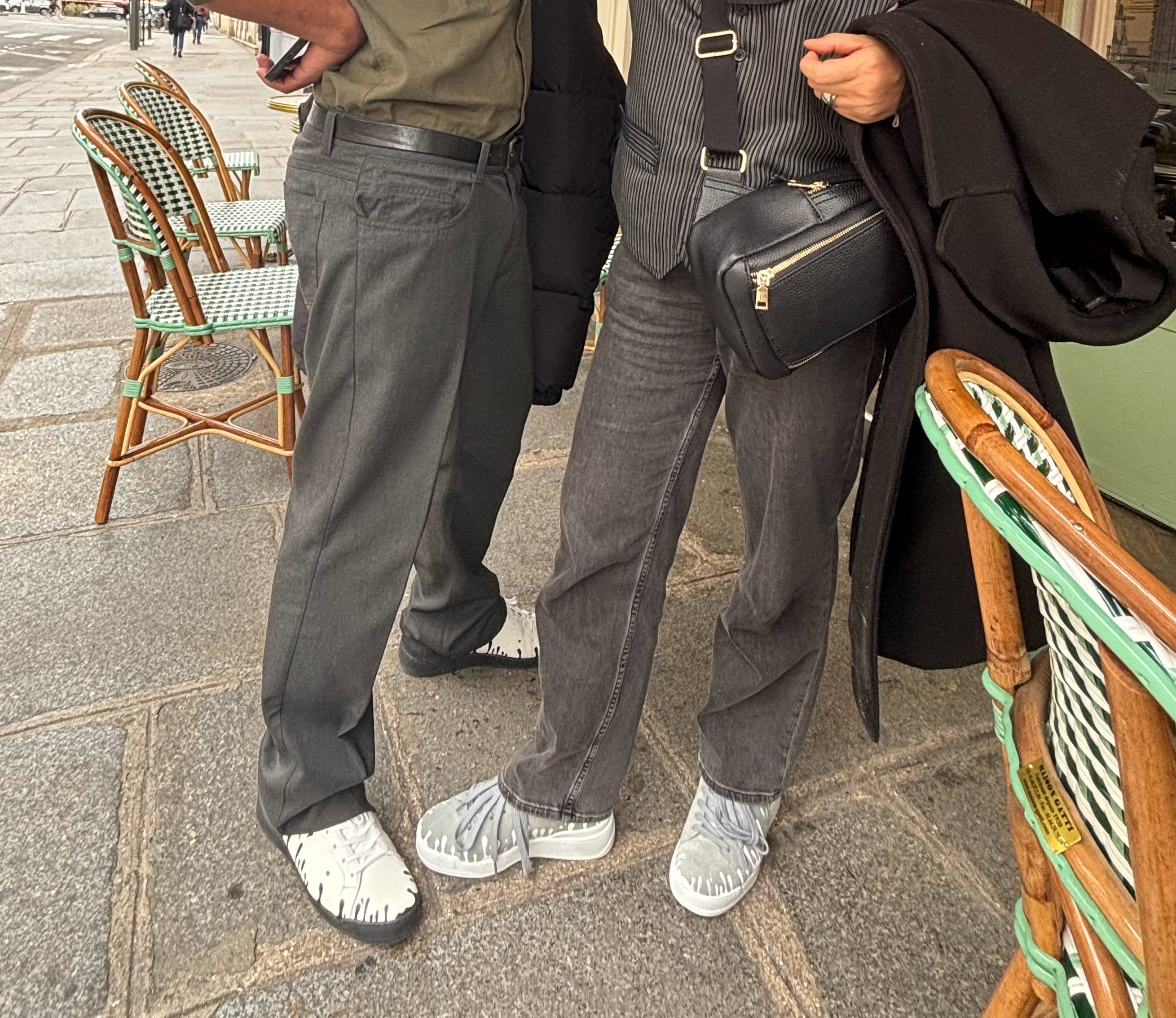 Pair of white Nappa leather low-top sneakers with exclusive printed black drops design and black soles worn with grey pants and pair of grey suede low-top sneakers with exclusive printed white drops design and white soles worn with grey jeans