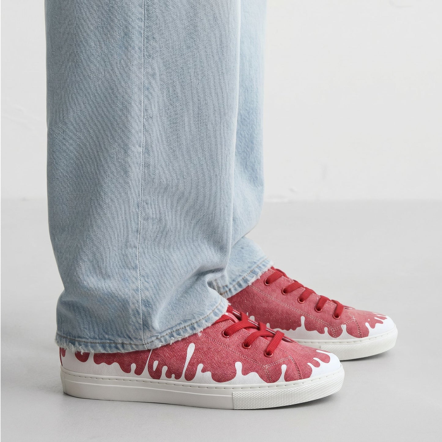 33MB low-top Sunset raspberry red recycled canvas sneakers featuring the Zero Gravity® upward-drop motif representing hope  with white soles,  worn with light blue jeans on a plain background