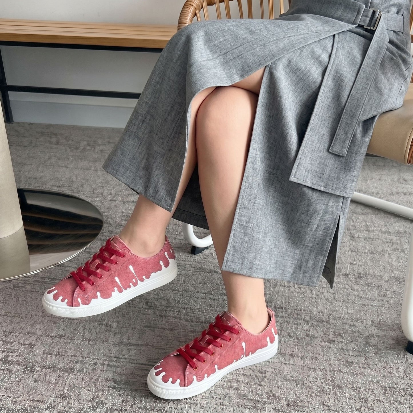 Person wearing a grey long skirt with a belt, with 33MB low-top Sunset raspberry red recycled canvas sneakers featuring the Zero Gravity® upward-drop motif representing hope  with white soles,  on a carpeted floor.