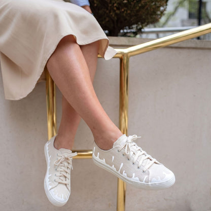 Person wearing 33MB Mirage sandy recycled canvas sneakers featuring the Zero Gravity® upward-drop motif representing hope  worn with a beige skirt on a wall with a golden ramp