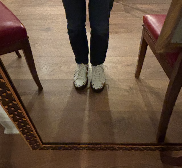 Person wearing black pants and 33MB Yang white leather sneakers featuring the Zero Gravity® upward-drop motif in front of a mirror on a  wooden floor