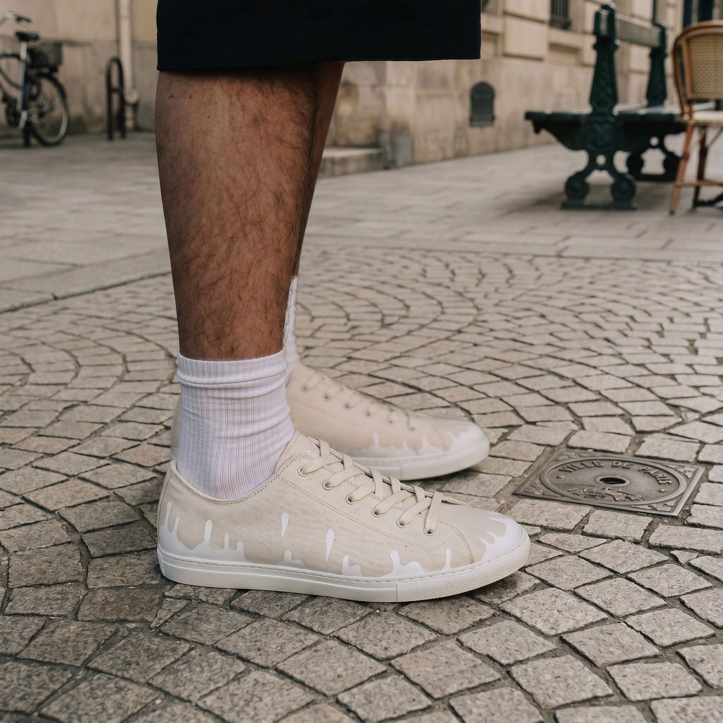 A person wearing black shorts, and off-white cream low-top 33MB sneakers featuring the Zero Gravity unique upward drip motif design near the soles representing hope. 