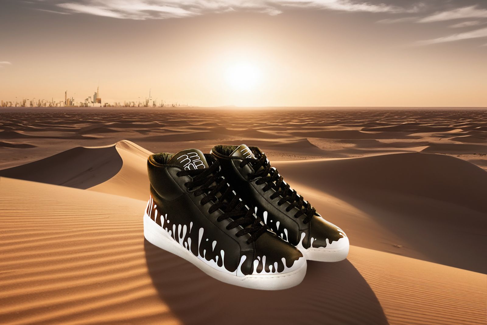 Pair of black Nappa leather mid-top sneakers with exclusive printed white drops design and white soles on desert sand with city highline in the background