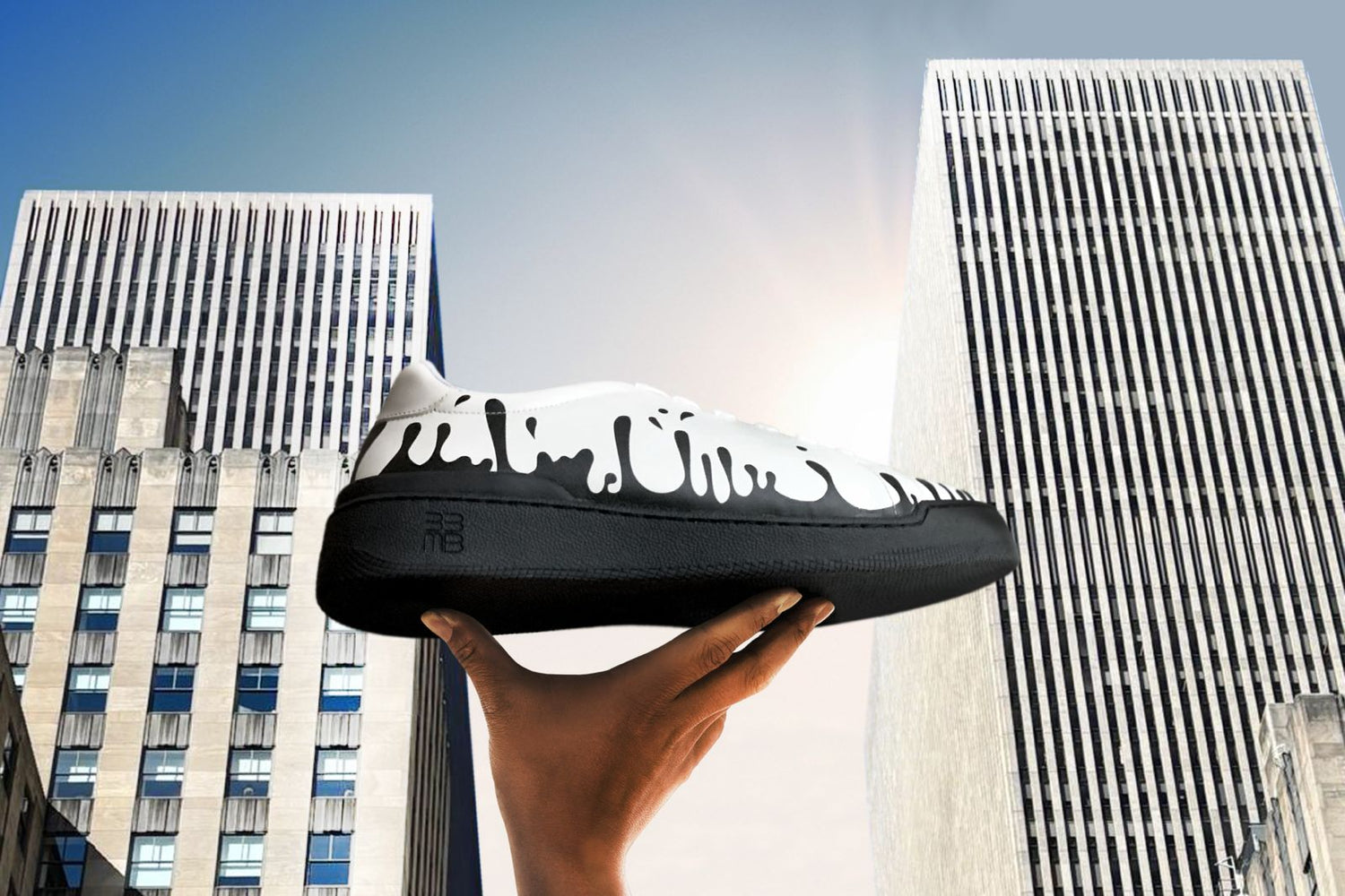 White Nappa leather low-top sneaker with exclusive printed black drops design and black sole held in front of skycrapers