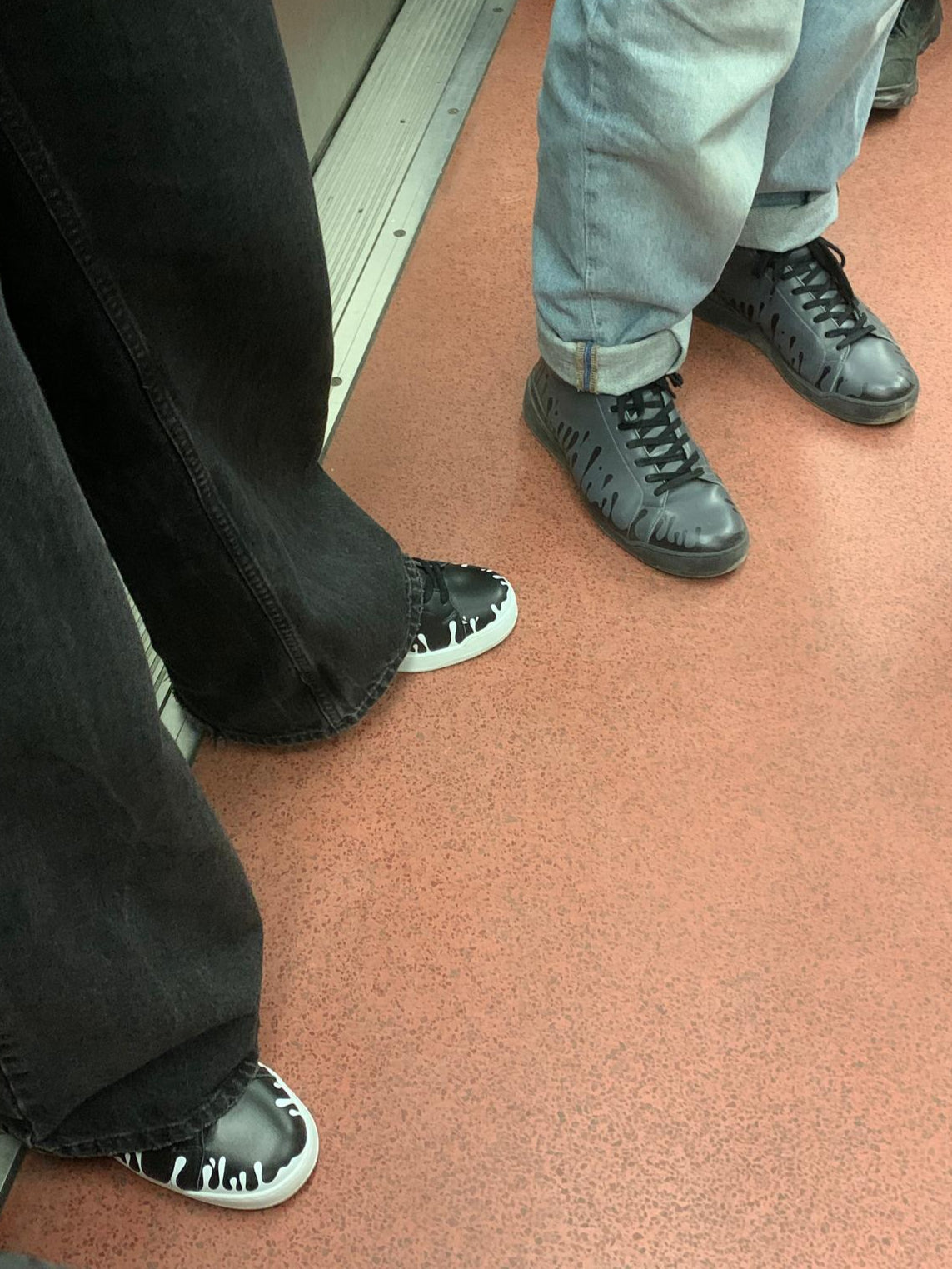 Pair of black Nappa leather mid-top sneakers with exclusive printed white  drops design on white soles worn with black pants and pair of dark grey Nappa leather mid-top sneakers with exclusive printed black drops design and black soles worn with blue jeans
