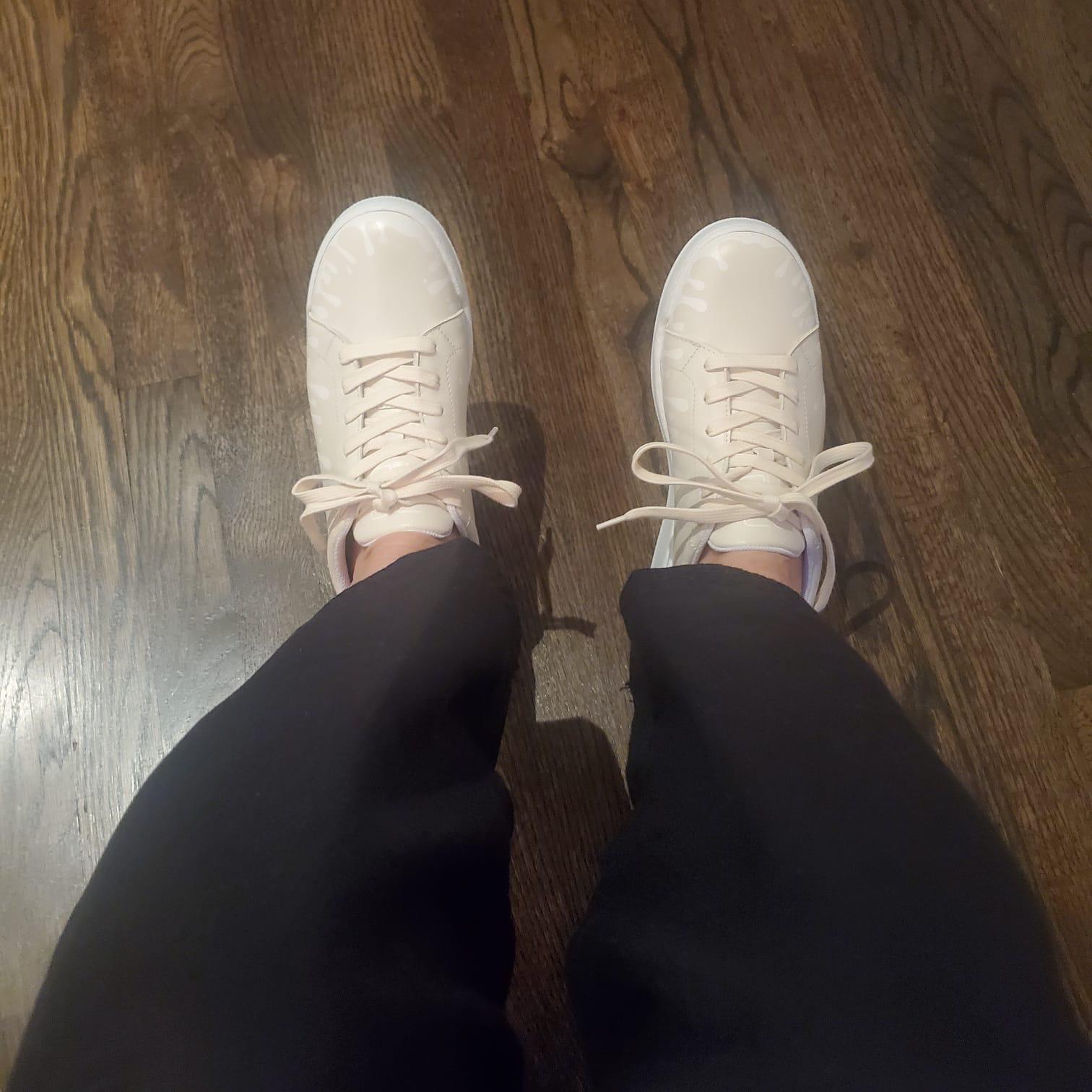 Cream color sneakers with exclusive drip design worn with black pants on wooden floor