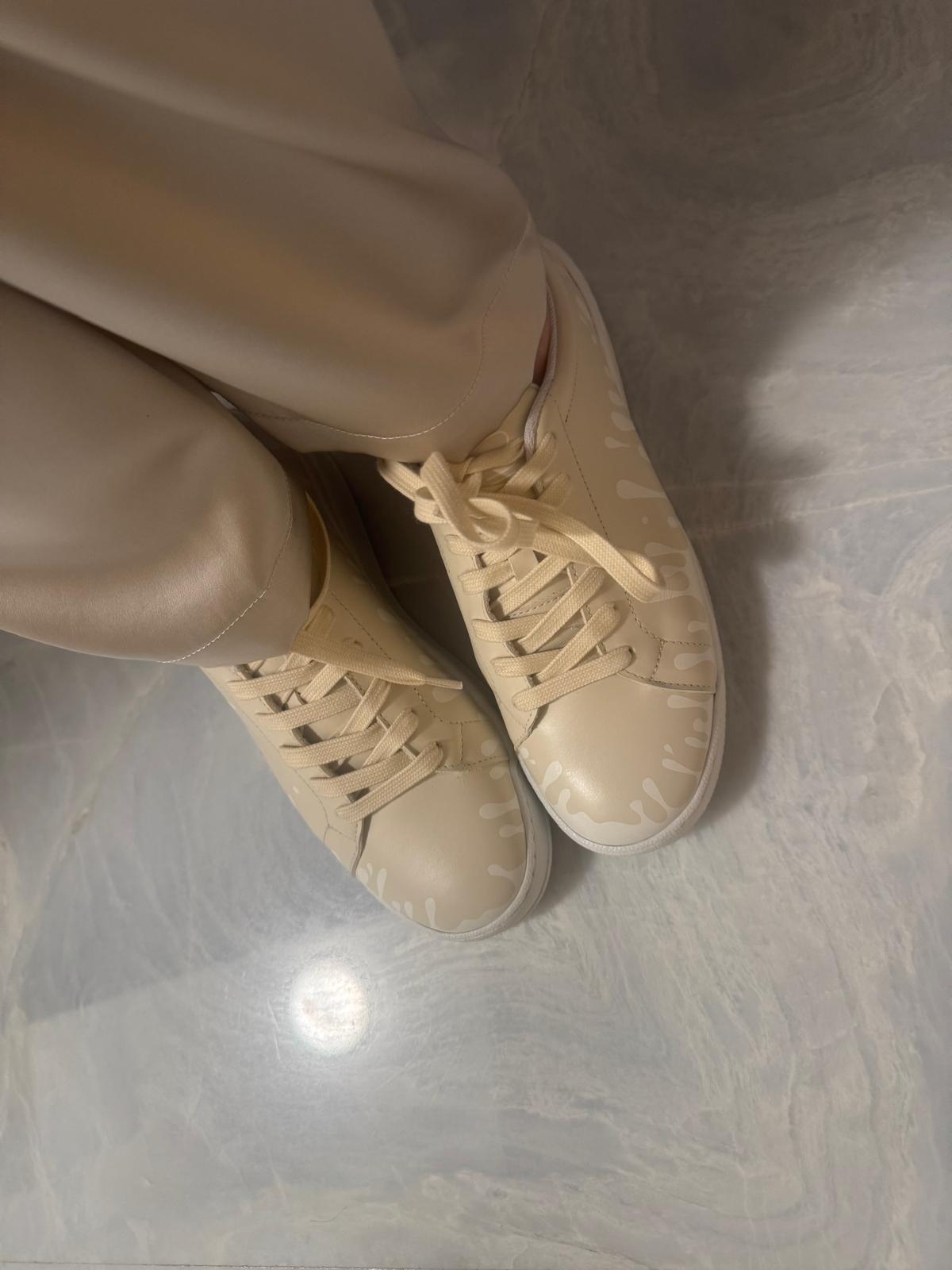 Cream color Nappa leather low-top sneakers with exclusive printed white drops design and white soles worn with beige pants on marble floor