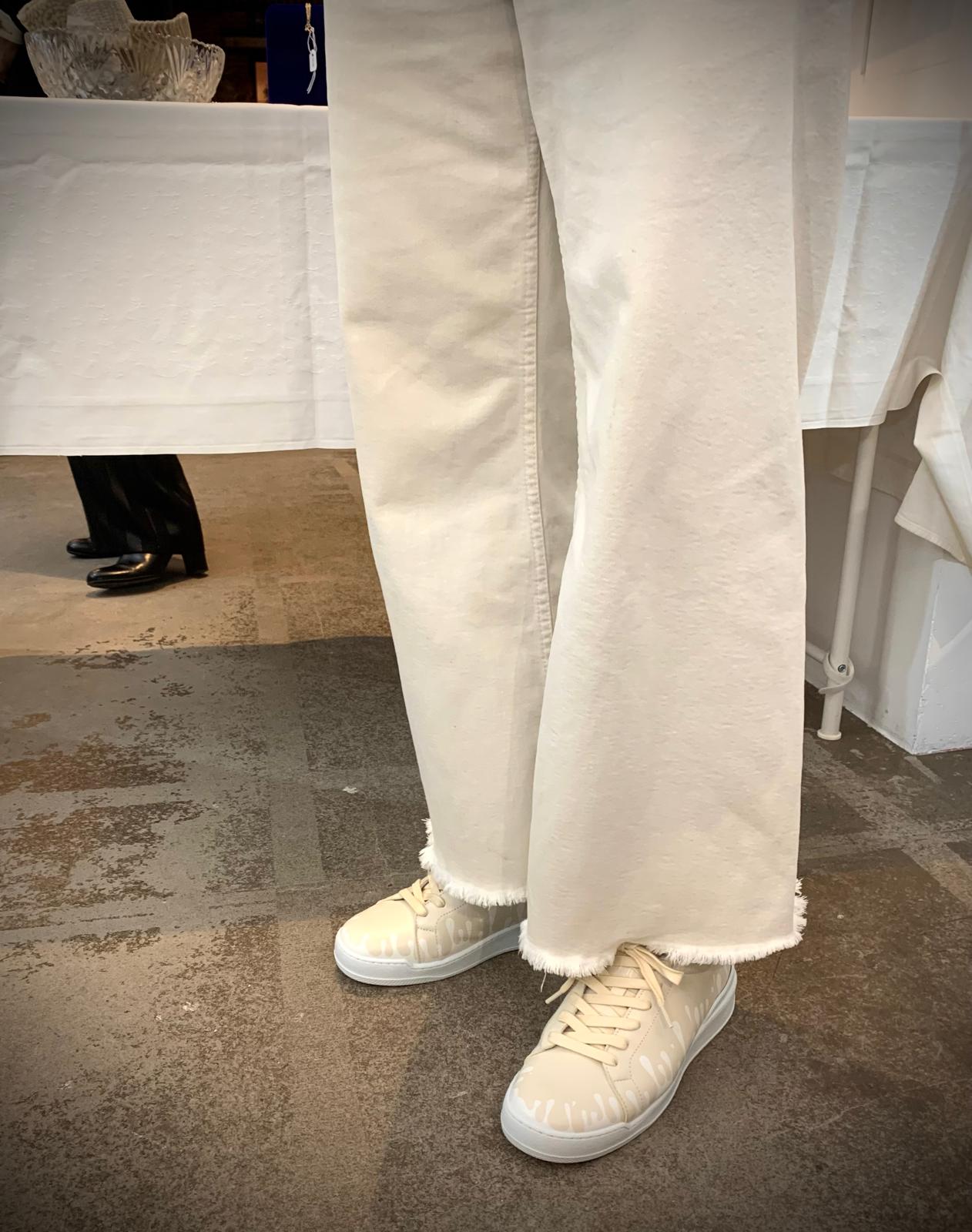 Person wearing White jeans and 33MB Dawn cream sneakers featuring the Zero Gravity® upward-drop motif on a stone floor.