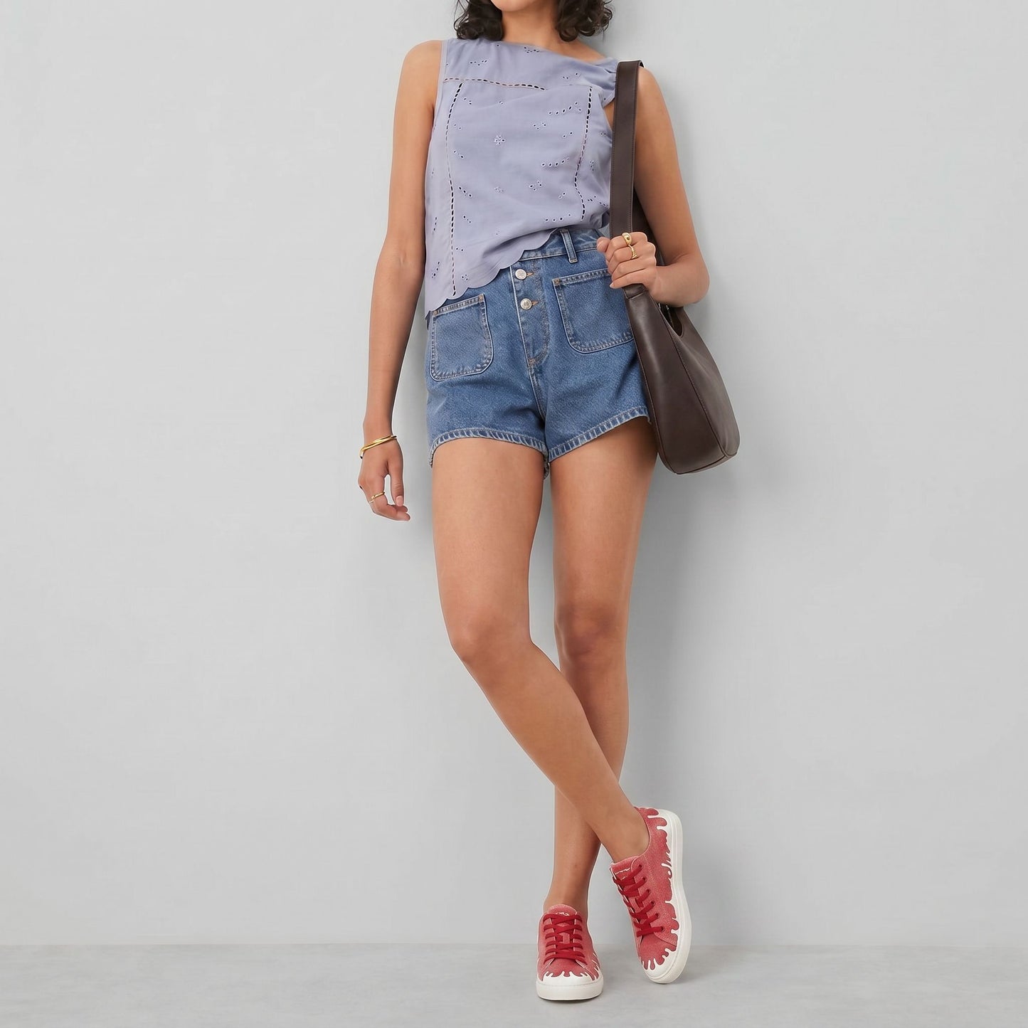 Person wearing a light grey sleeveless top, blue denim shorts, and  33MB low-top Sunset raspberry red recycled canvas sneakers featuring the Zero Gravity® upward-drop motif representing hope  with white soles, carrying a brown shoulder bag against a light gray studio background. 