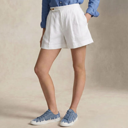 A person wearing white high-waisted linen shorts, a blue button-down shirt, and 33MB low-top Zephyr denim blue recycled canvas sneakers featuring the Zero Gravity® upward-drop motif representing hope  with white soles,  standing against a neutral beige textured background.