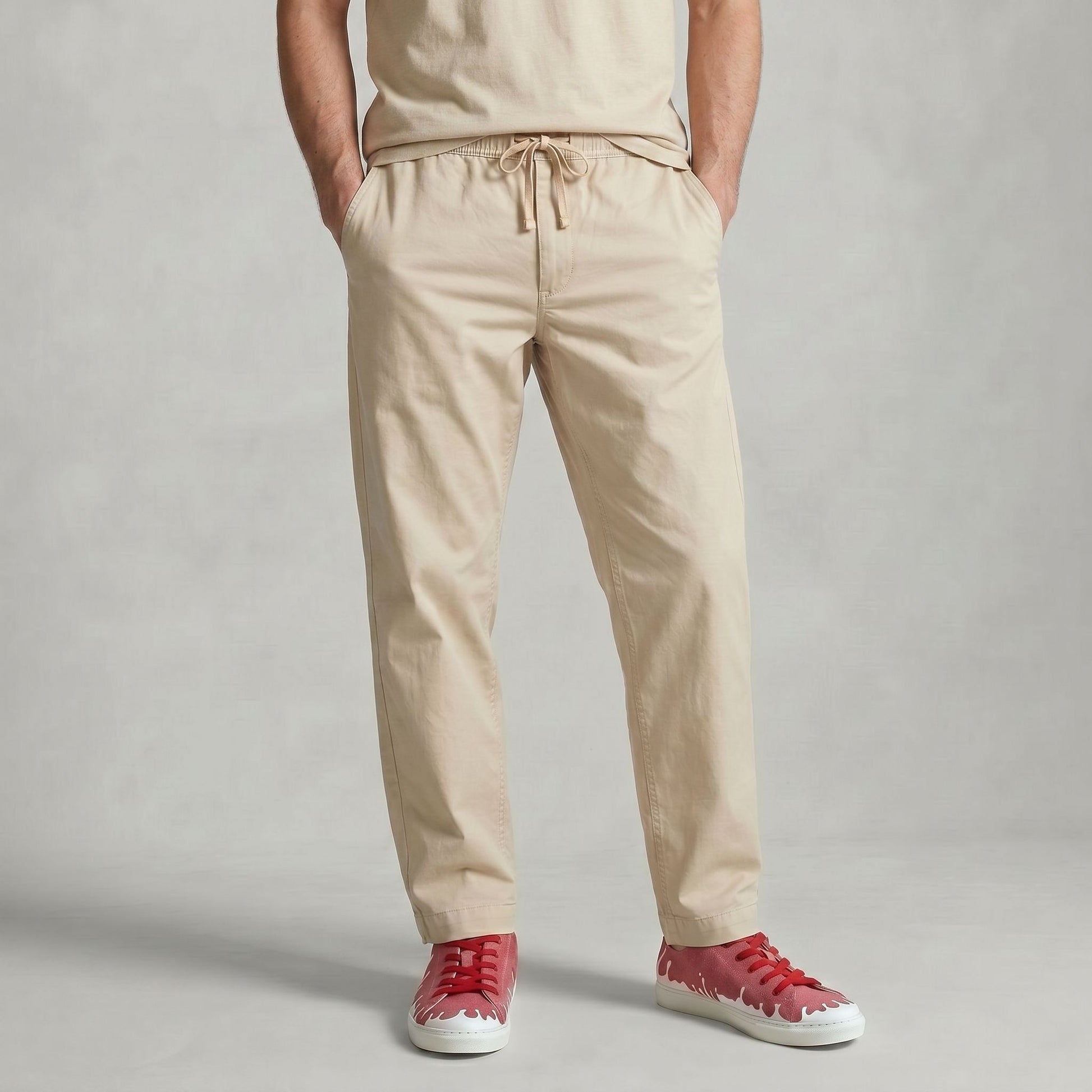 A person wearing beige drawstring trousers with hands in pockets, paired with a matching beige top and  33MB low-top Sunset raspberry red recycled canvas sneakers featuring the Zero Gravity® upward-drop motif representing hope  with white soles,  standing against a light gray backdrop.