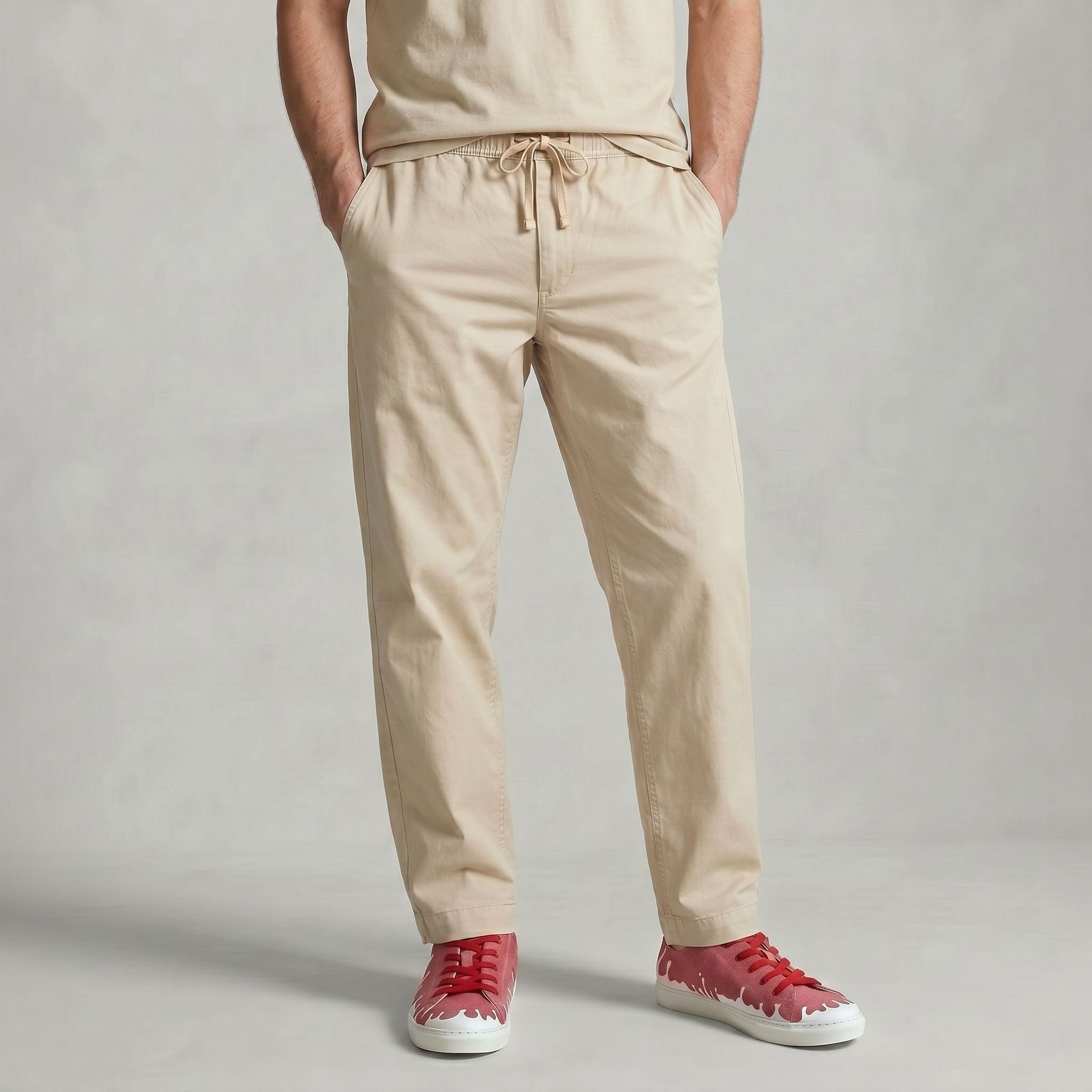 A person wearing beige drawstring trousers with hands in pockets, paired with a matching beige top and  33MB low-top Sunset raspberry red recycled canvas sneakers featuring the Zero Gravity® upward-drop motif representing hope  with white soles,  standing against a light gray backdrop.
