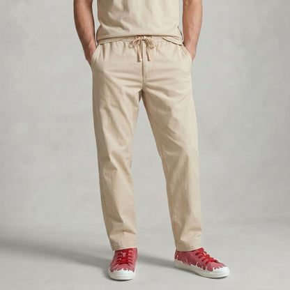 A person wearing beige drawstring trousers with hands in pockets, paired with a matching beige top and  33MB low-top Sunset raspberry red recycled canvas sneakers featuring the Zero Gravity® upward-drop motif representing hope  with white soles,  standing against a light gray backdrop.
