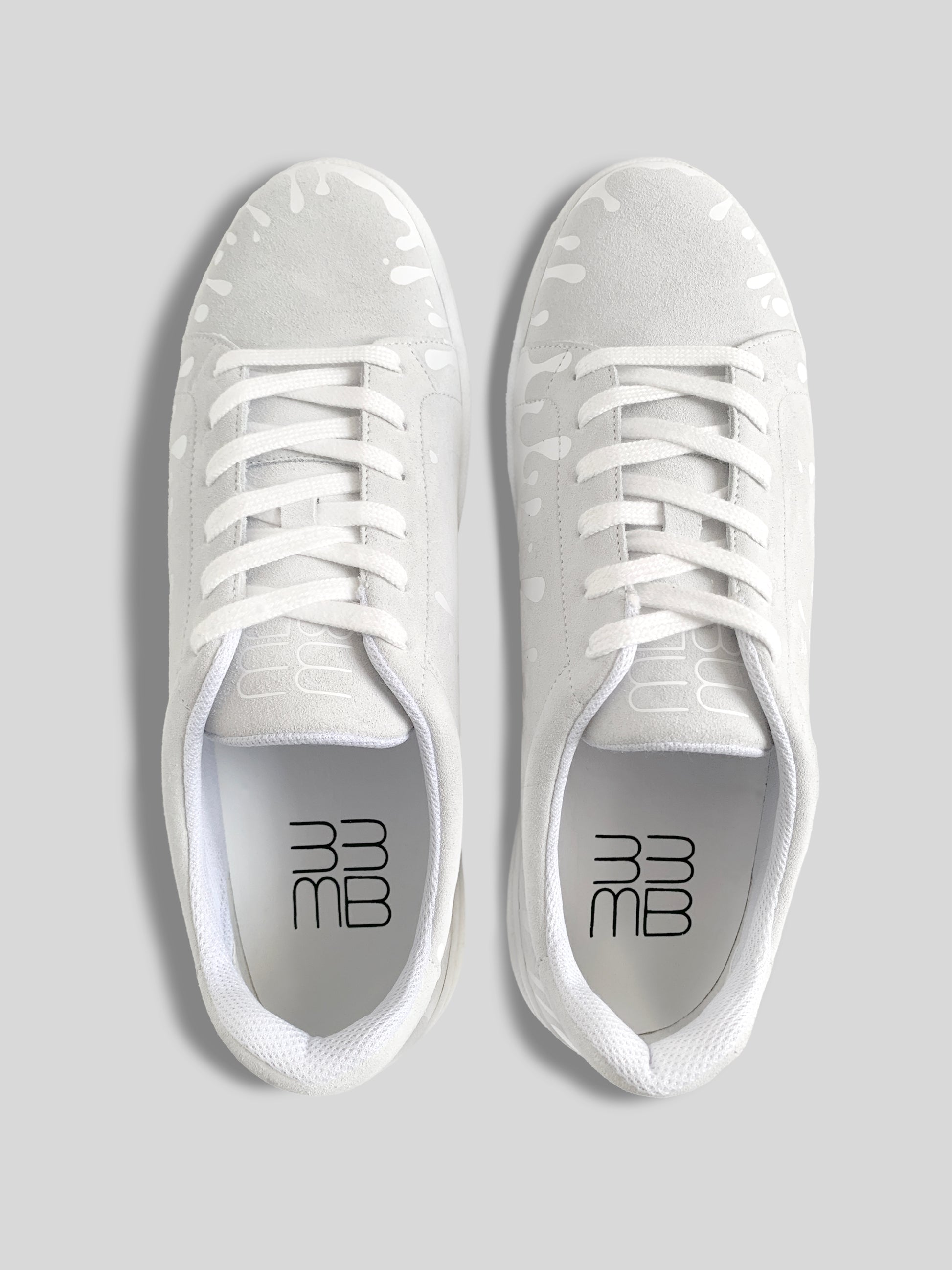 Top view of pair of white suede low-top sneakers with exclusive printed white drops design