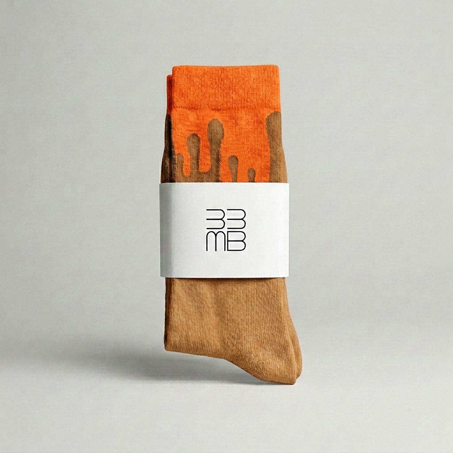 Folded 33MB premium organic cotton crew socks featuring a white brand band with the 33MB logo and the Zero Gravity® signature motif of camel paint droplets flowing upward toward the orange cuff to symbolize hope and constant positivity.