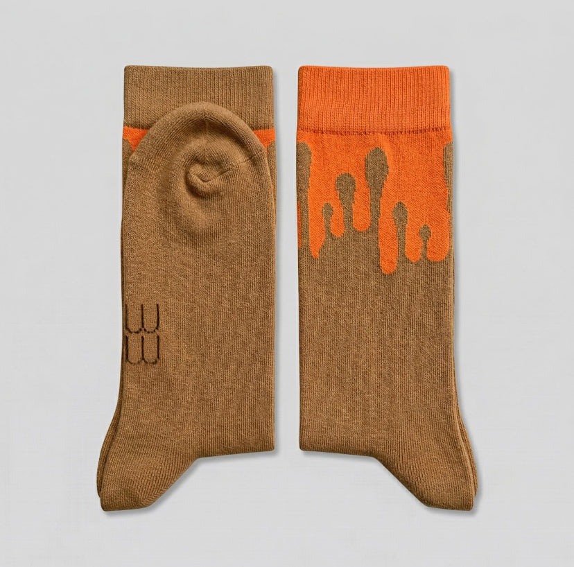 Folded 33MB premium organic cotton crew socks featuring the Zero Gravity® motif with camel paint droplets flowing upward toward the orange cuff, to symbolize hope and constant positivity.