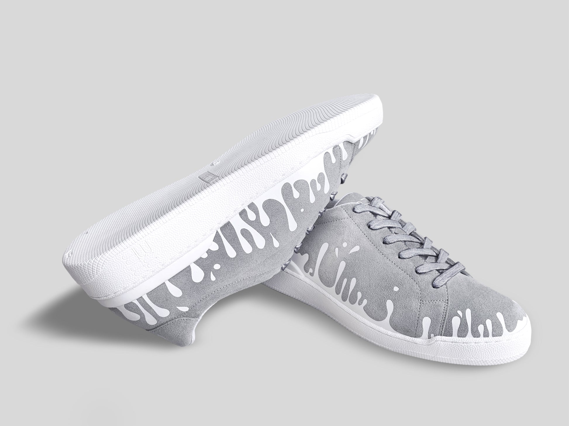 Upside down view of grey suede low-top sneakers with exclusive printed white drops design and white soles