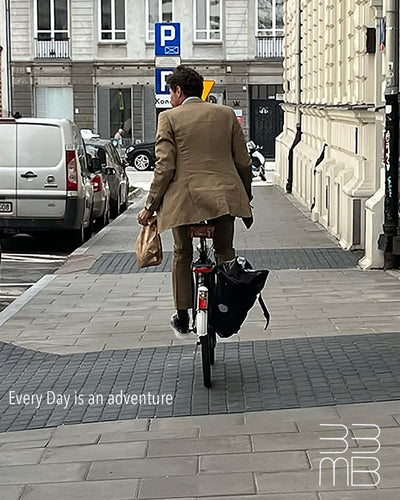 Person riding a bicycle on a city street wearing black leather sneakers with white drop design with a 'Every Day is an adventure' quote and logo.